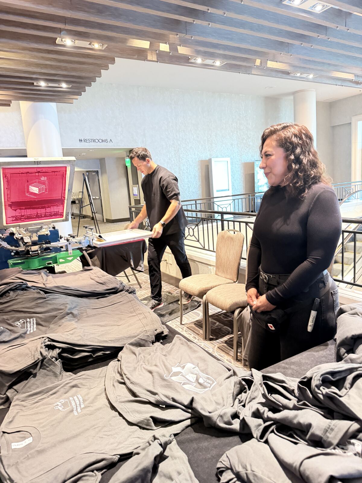 Indoor event booth with printing equipment and staff displaying merchandise at the table