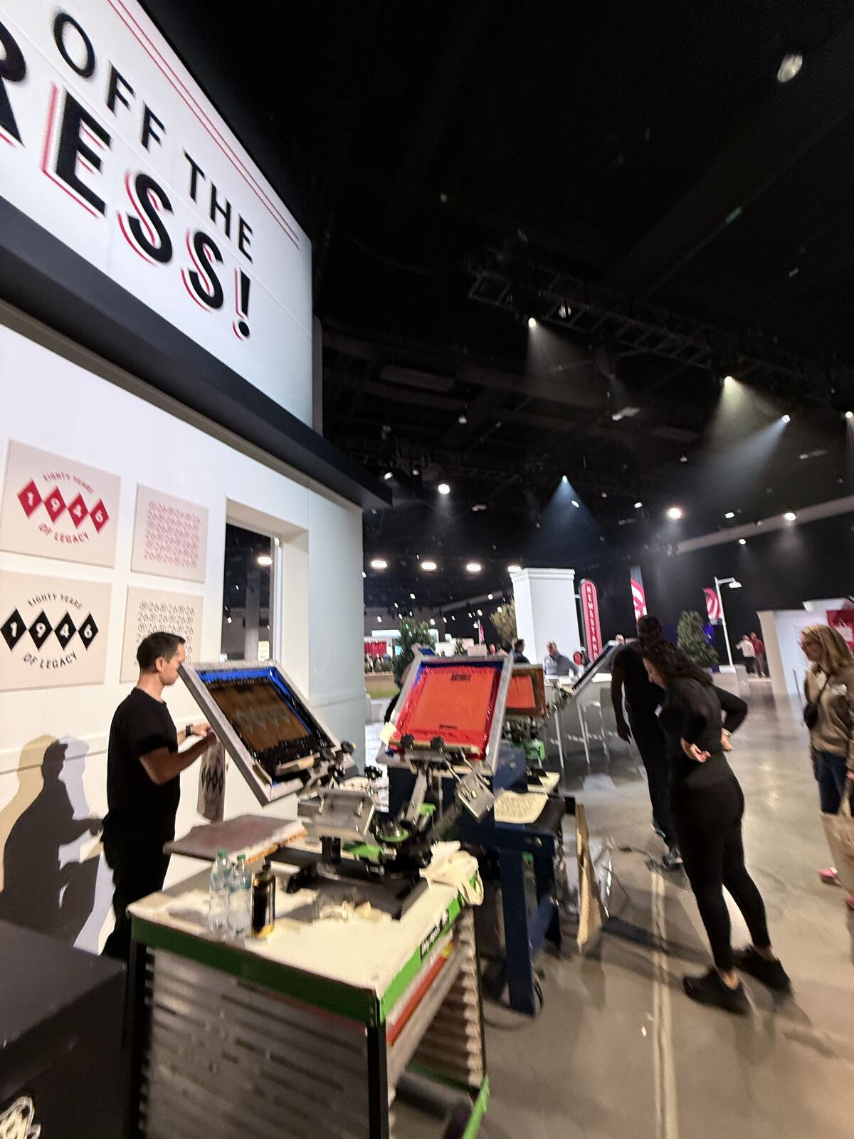 Overhead shot of an indoor event space with guests browsing printed merchandise samples on tables